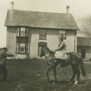 Olive Burgess on horse in front of farmhouse