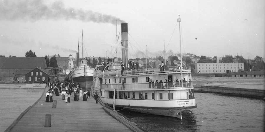 A ship bearing the name King Edward of St. John's N.F. on it's hull is docked in Kincardine Harbour. There is a large crowd walking on the pier, and passengers are standing on the ship's three decks. The rear range lighthouse, Coombe Furniture Factory, the Methodist Church and other buildings are in the distance.