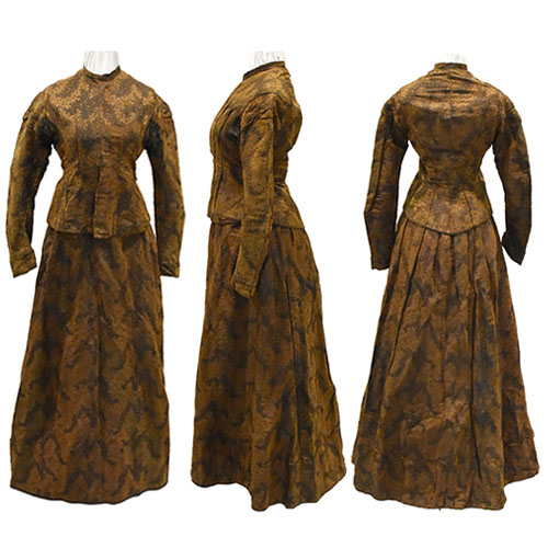 A Victorian-era 2-pieve gown, consisting of a fitted jacket and long skirt. They brown with a gold and black brocade pattern. The back of the skirt is pleated to accommodate a bustle.
