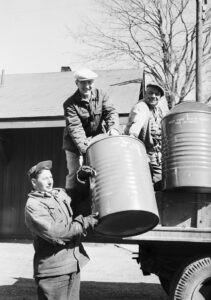 Three men handling large metal barrels